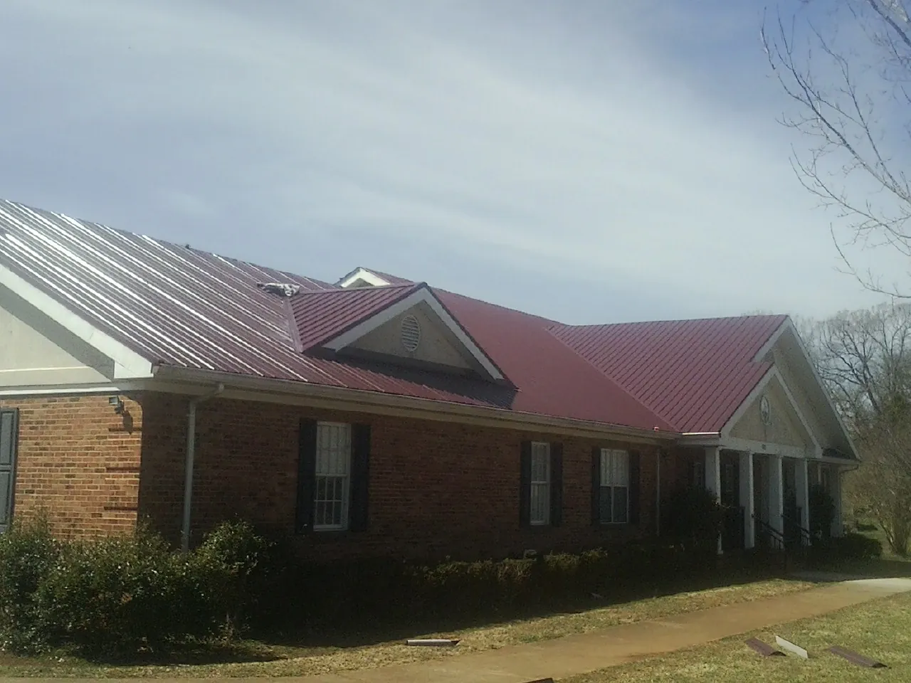 Red metal roof with gabled entries on a long brick building, from a Hail Damage Roof Repair job in Rosenberg