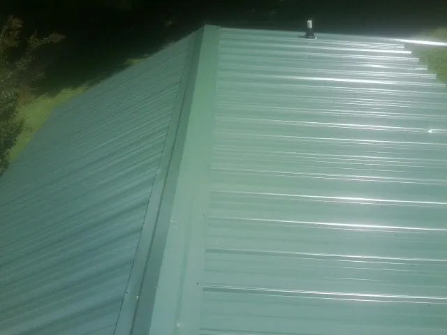 New green metal panels meeting at the ridge of a roof — Flat Roof Repair work by our crew in Rosenberg