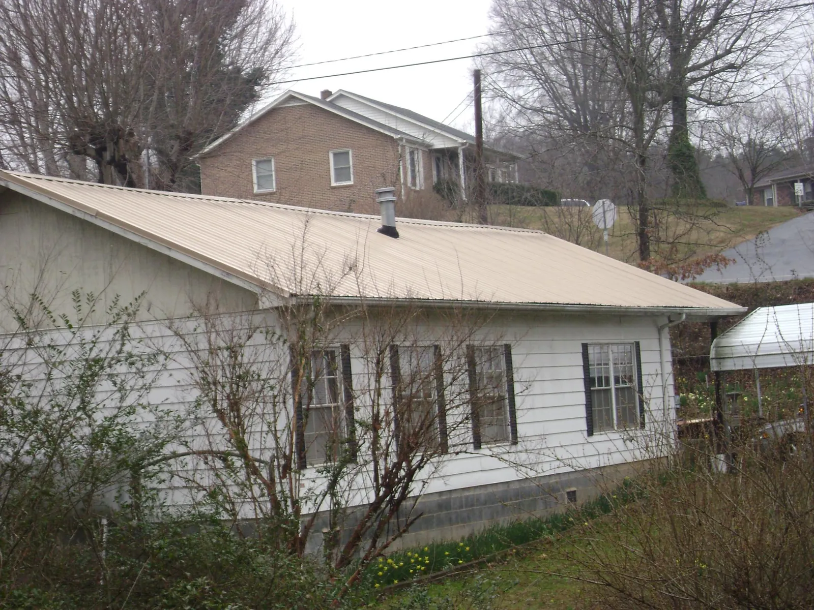 Tan metal roof on a white sided house set into a hillside — Commercial Roofing by Roofing Brothers in Rosenberg